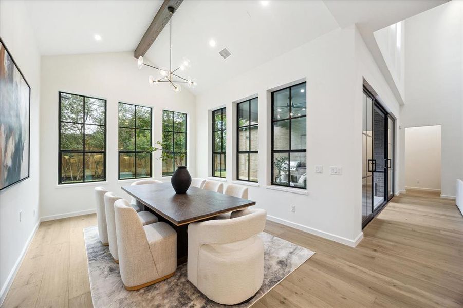 The spacious dining area features an elegant chandelier, vaulted ceiling, and large windows, allowing for both natural light and privacy.