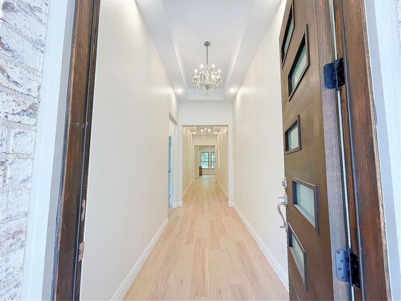 Grand entry with chandeliers, a wide hallway, & white oak colored flooring