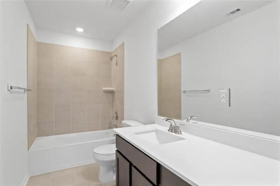 The secondary bathroom showcases tile flooring, a bath/shower combo with a Silver Gray Daltile tile surround, a 36" vanity with a stunning light countertop, a stylish mirror, sleek fixtures, and contemporary finishes throughout.