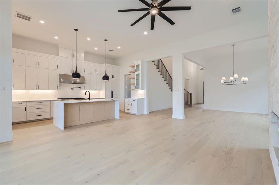 Kitchen featuring light wood-type flooring, ceiling fan with notable chandelier, white cabinetry, a center island with sink, and decorative light fixtures