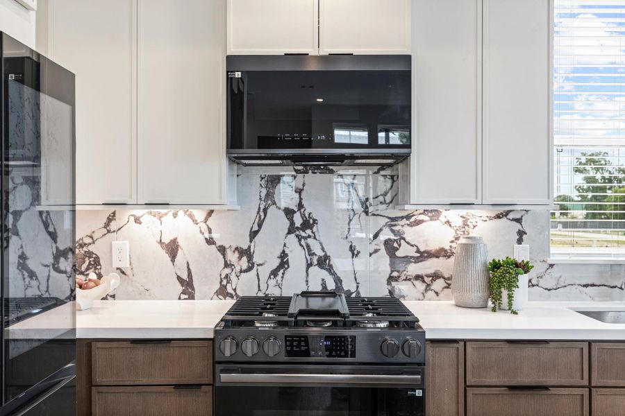 Sleek and modern kitchen featuring elegant marble-patterned backsplash, state-of-the-art appliances, and ample natural light for a sophisticated culinary experience. **Model of similar home**