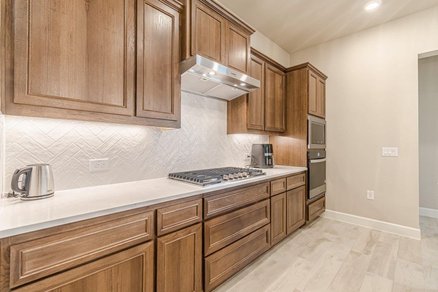 Kitchen featuring baseboards, stainless steel appliances, tasteful backsplash, and under cabinet range hood