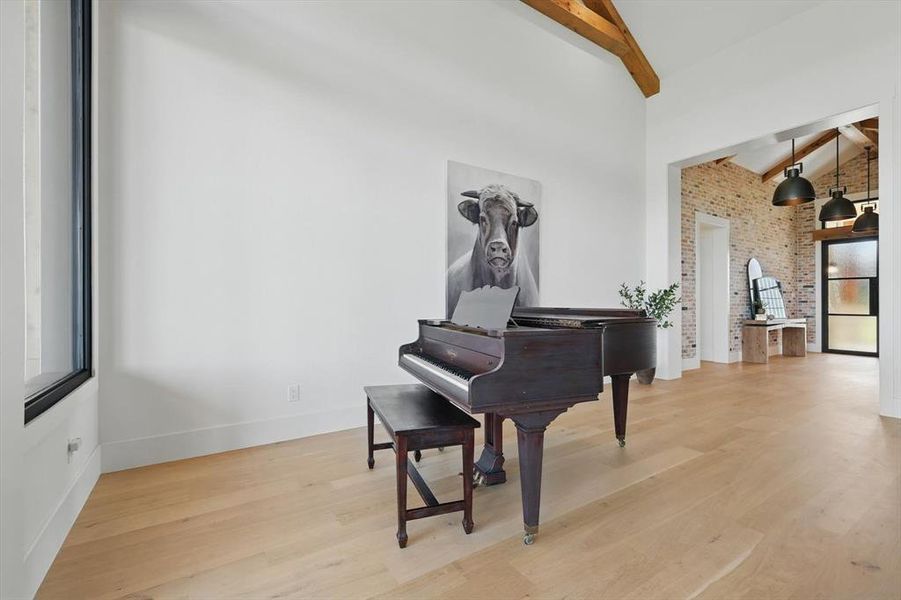 Sitting room with beamed ceiling, brick wall, light wood-style flooring, high vaulted ceiling, and healthy amount of natural light Sitting room with beamed ceiling, brick wall, light wood-style flooring, high vaulted ceiling, and healthy amount of natural light