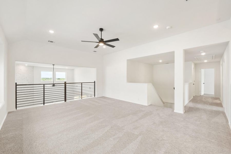Open upstairs loft with carpet flooring, ceiling fan, and metal railing overlooking lower level
