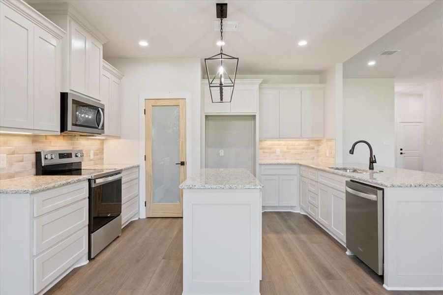 Kitchen with decorative backsplash, stainless steel appliances, white cabinets, light stone countertops, and a peninsula Kitchen with decorative backsplash, stainless steel appliances, white cabinets, light stone countertops, and a peninsula