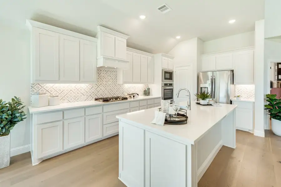 Kitchen with white cabinets, large center island, patterned tile backsplash, and stainless steel appliances on light wood floors