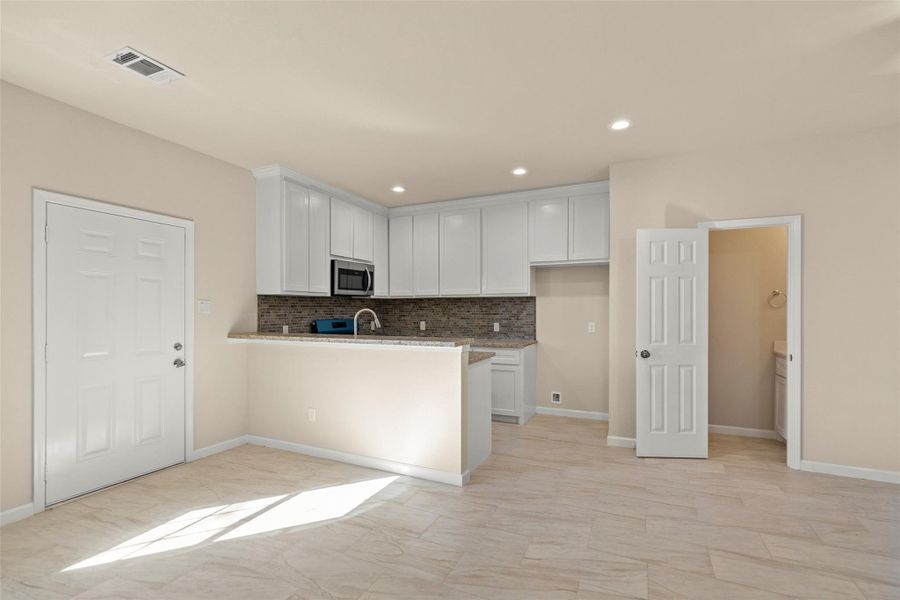 Spacious open-plan living area with neutral tones, featuring tile flooring and recessed lighting. The room includes a modern kitchen with stainless steel appliances and white cabinetry. A ceiling fan and natural light from the window enhance the space.