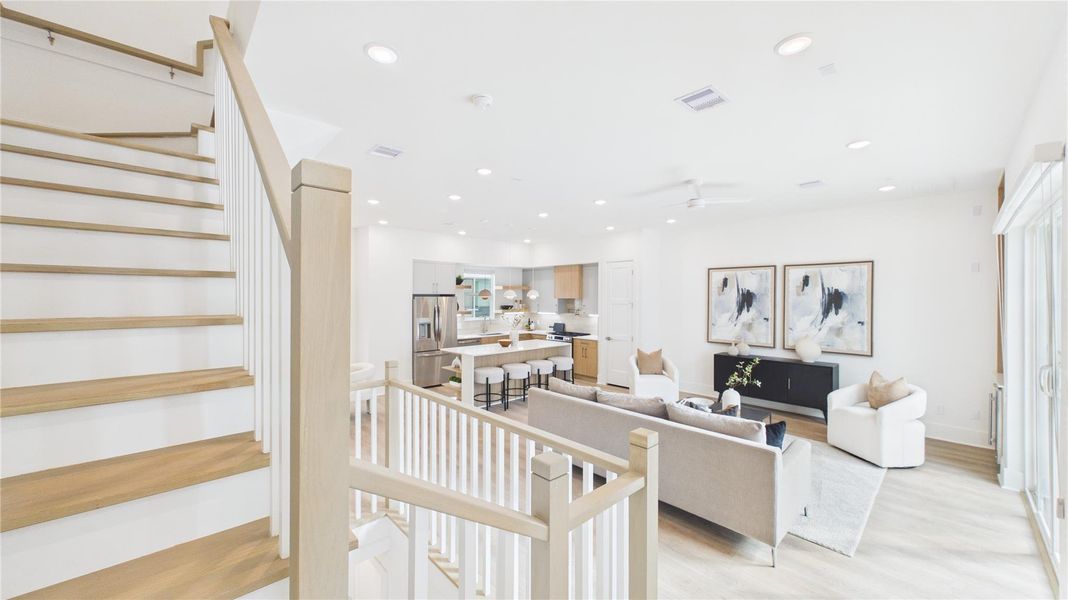 This modern, open-concept living space features a bright, airy design with light wood flooring, a stylish kitchen with stainless steel appliances, and comfortable seating. The staircase adds elegance, while large windows ensure plenty of natural light.