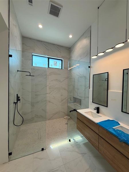 Bathroom featuring double vanity, a marble finish shower, light marble finish flooring, and recessed lighting