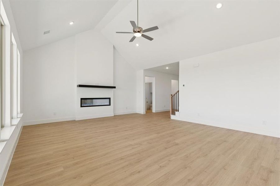 Unfurnished living room with a glass covered fireplace, light wood-style flooring, high vaulted ceiling, a ceiling fan, and recessed lighting