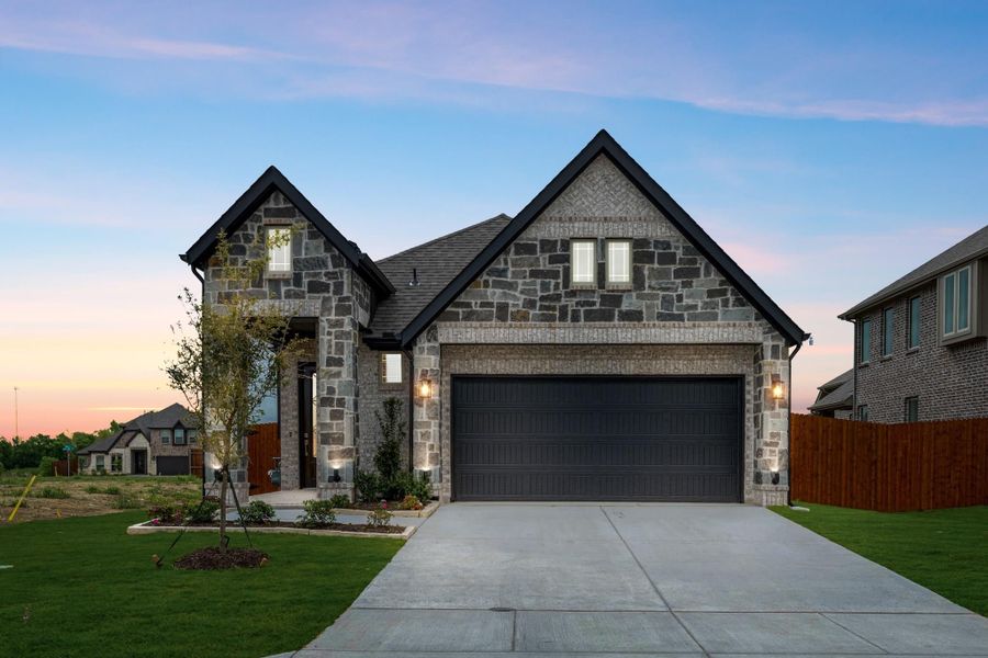 Two-story home with stone and brick exterior, two-car garage, and concrete driveway at dusk