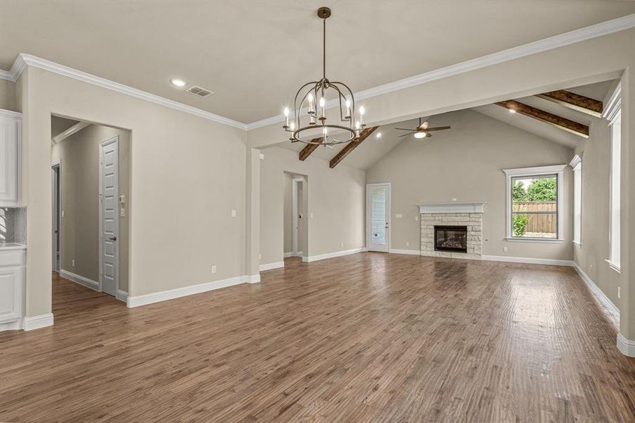 Unfurnished living room with hardwood / wood-style floors, crown molding, a fireplace, vaulted ceiling with beams, and ceiling fan with notable chandelier