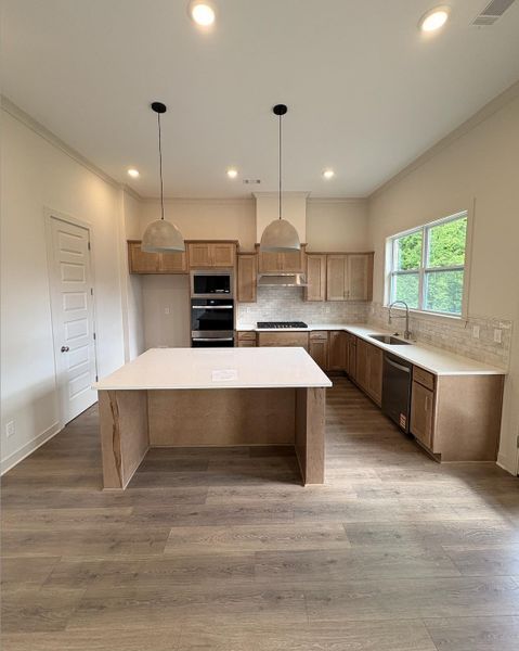 Kitchen featuring an expansive center island with a light-toned countertop, wood-finish flooring, recessed lighting, and pendant fixtures