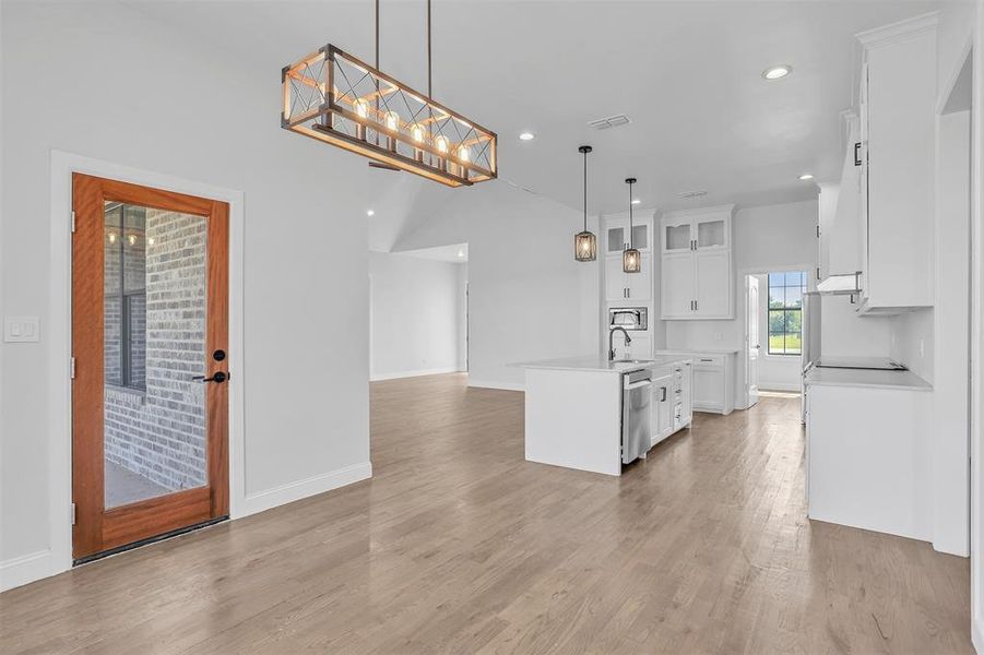 Kitchen featuring white cabinetry, stainless steel appliances, pendant lighting, an island with sink, and light hardwood / wood-style flooring