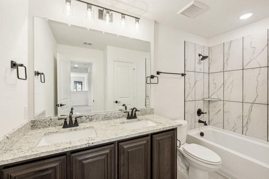Bathroom with double sink granite vanity, dark cabinets, and tub-shower with marble tile surround