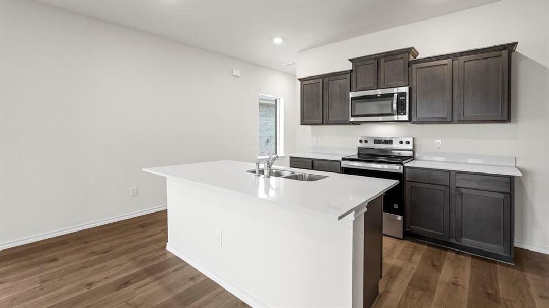 The kitchen features a central island with a sink, white countertops, and dark wood cabinetry with stainless steel appliances