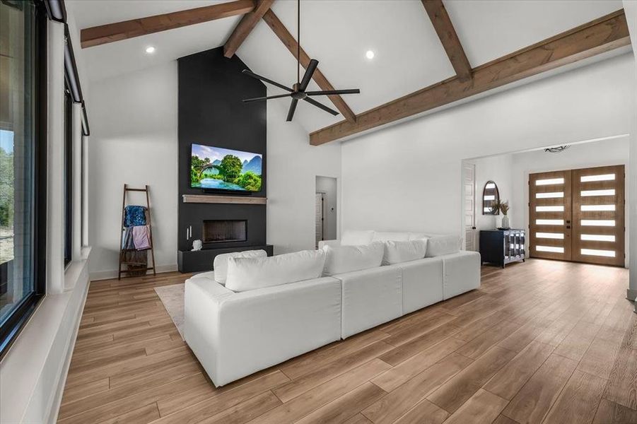 Vaulted living room with stained box beams and floor to ceiling black tile hearth with floating mantle and propane/wood burning fireplace.