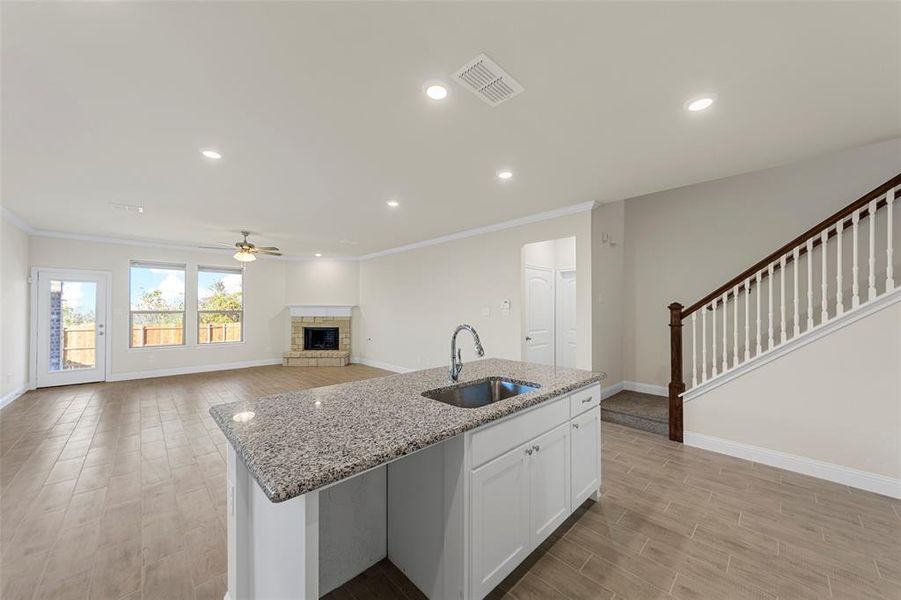 Kitchen with a center island with sink, sink, ceiling fan, light stone counters, and white cabinetry