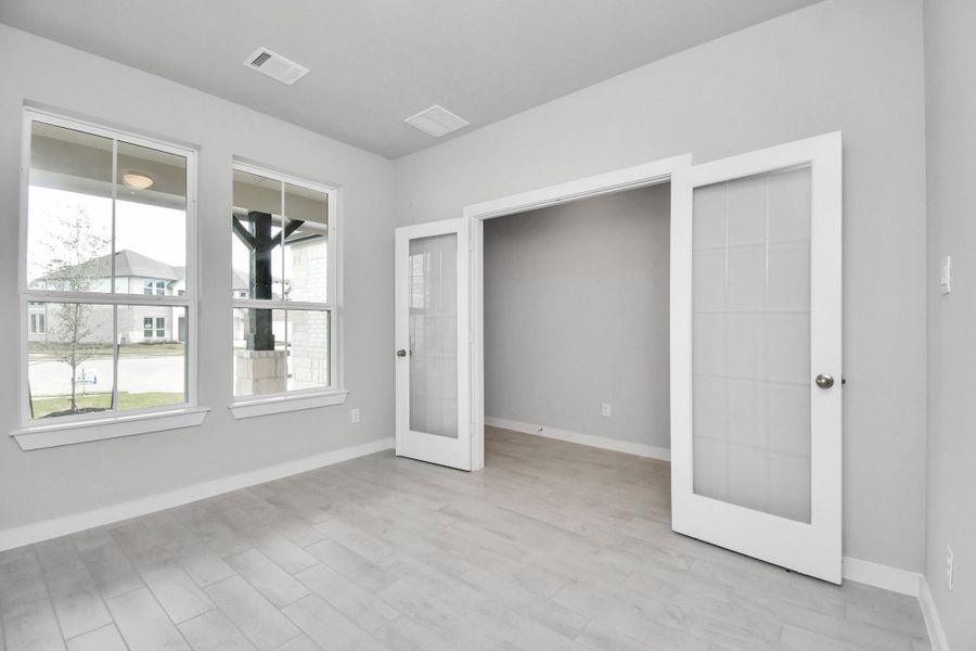Experience the perfect blend of sophistication and warmth in this home office, boasting elegant wood-look tile flooring and flooded with natural light from expansive windows and French doors. Sample photo of completed home with similar floor plan. Actual colors and selections may vary.