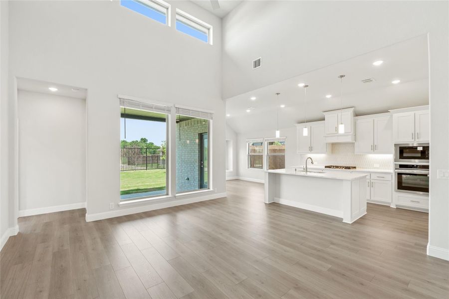 Open-concept living area and kitchen with high ceilings, white cabinets, center island, and hardwood floors Open-concept living area and kitchen with high ceilings, white cabinets, center island, and hardwood floors