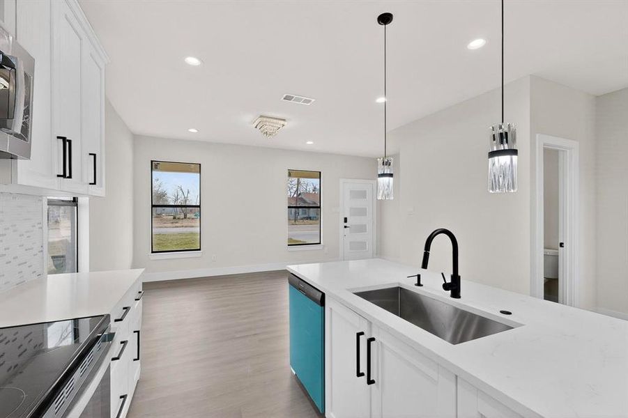 Dual tone kitchen with light stone countertops, light wood finished floors, pendant lighting, stainless steel microwave, and dishwasher Dual tone kitchen with light stone countertops, light wood finished floors, pendant lighting, stainless steel microwave, and dishwasher