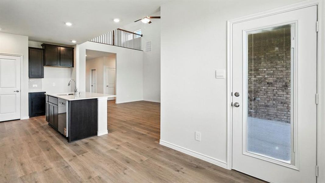 Open-concept living area featuring light wood flooring and a kitchen island with a sink Open-concept living area featuring light wood flooring and a kitchen island with a sink