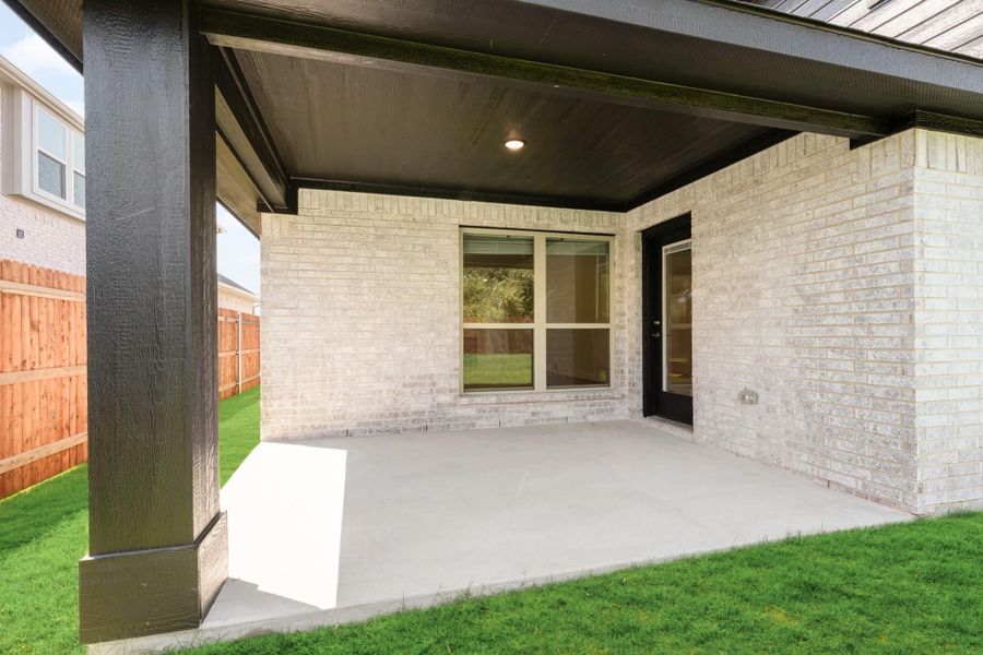 Covered back patio with concrete floor, white brick exterior, dark wood posts, and a wood privacy fence.
