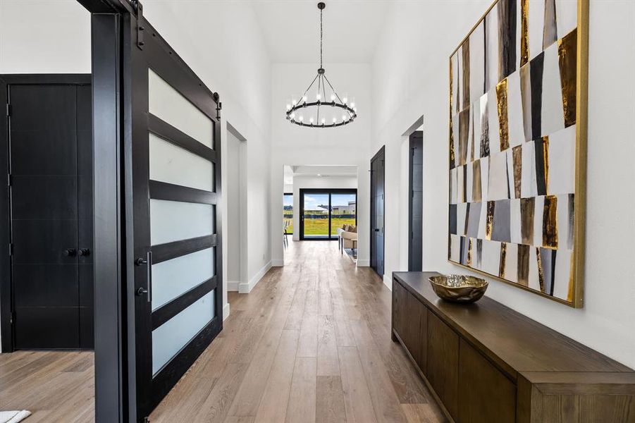 Hallway featuring a barn door, a high ceiling, light wood finished floors, and a chandelier