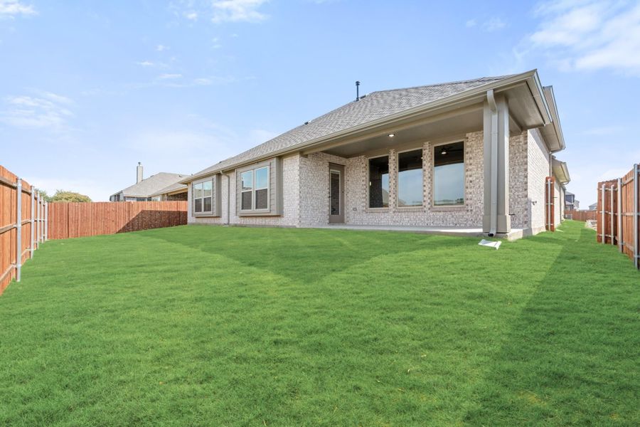 Backyard of brick home with covered patio, large green lawn, and wood privacy fence on both sides.