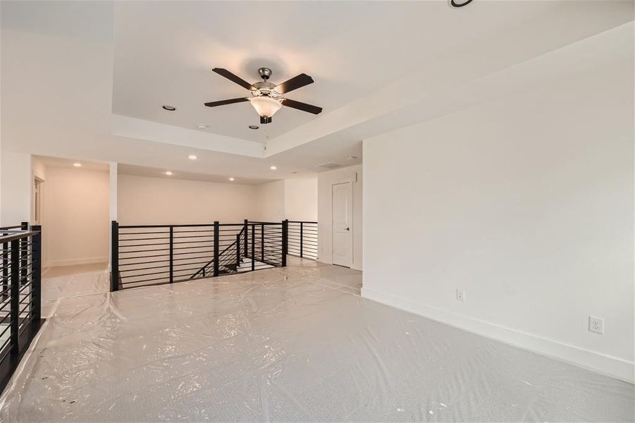 Empty room with ceiling fan and a tray ceiling