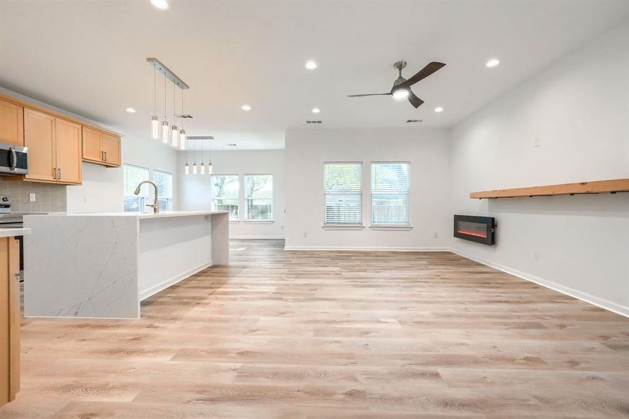 Unfurnished living room featuring recessed lighting, light wood finished floors, a glass covered fireplace, and ceiling fan