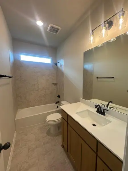 Bathroom featuring a single vanity with wood-finish cabinetry and a white countertop, coordinating tiled flooring, a bathtub with a tiled surround, and matte black fixtures