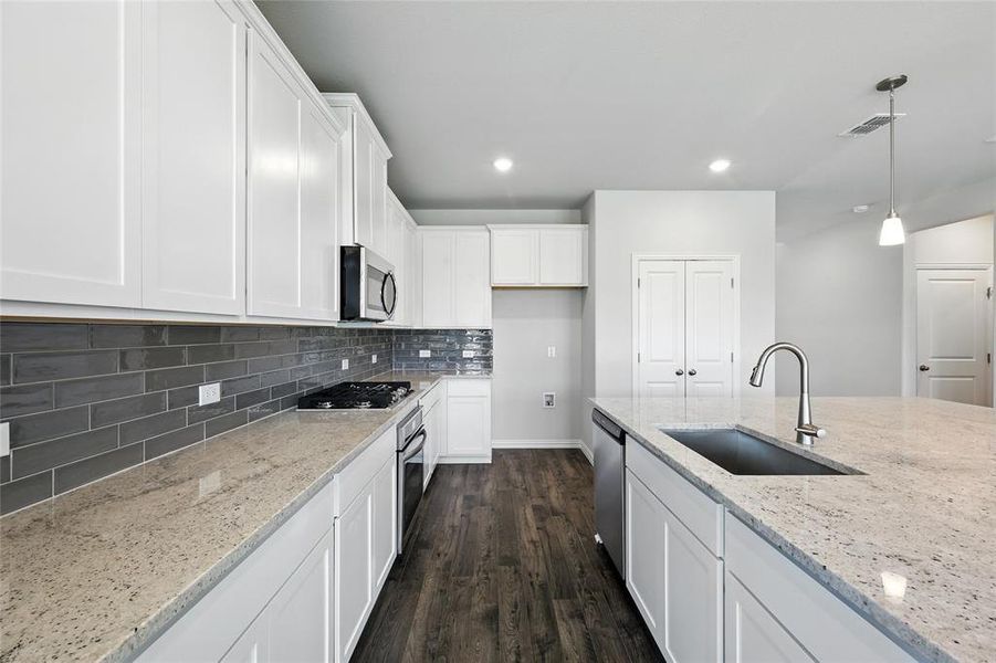 Kitchen with white cabinets, dark wood finished floors, hanging light fixtures, and light stone countertops