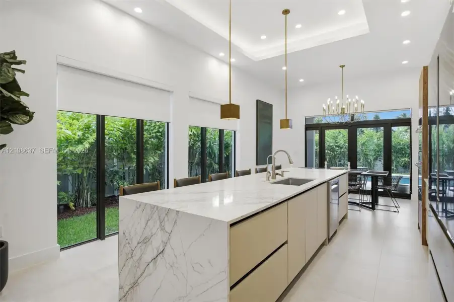 Kitchen featuring a waterfall-edge island with stone-finish countertops, ceiling-recessed lighting, dual hanging pendant lights, and floor-to-ceiling glass panel doors
