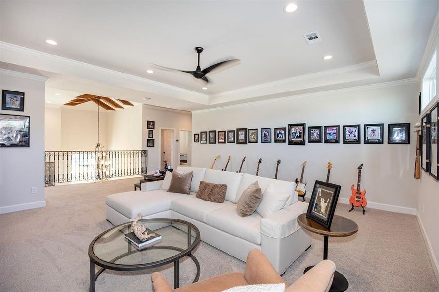 This spacious, carpeted living area features a cozy sectional sofa, modern ceiling fan, and ample natural light. Decorated with framed photos and guitars, it offers a stylish yet comfortable ambiance. The open railing provides a view to the lower level, enhancing the room's airy feel.