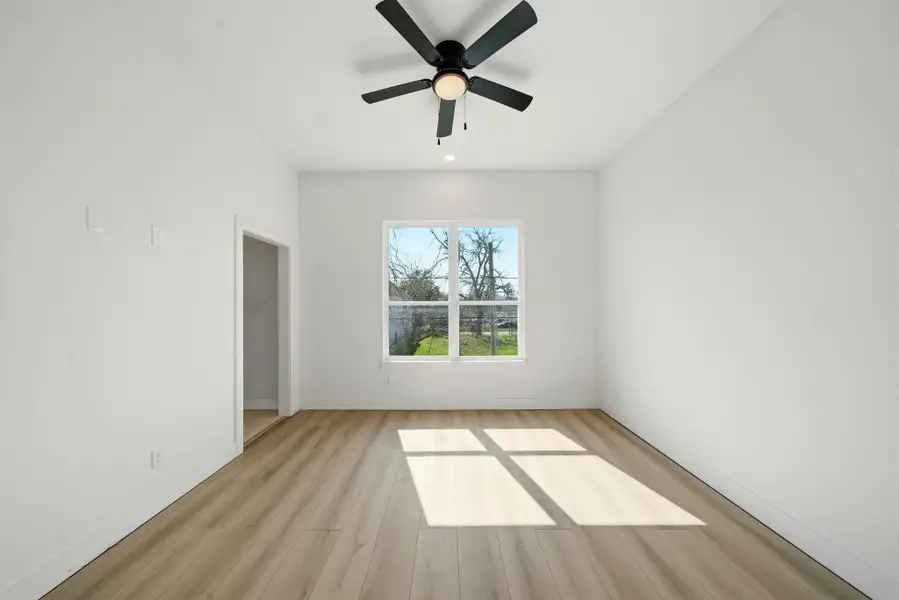 Bright, spacious room featuring large window with natural light, modern ceiling fan, and light wood flooring. Ideal for a bedroom or home office.