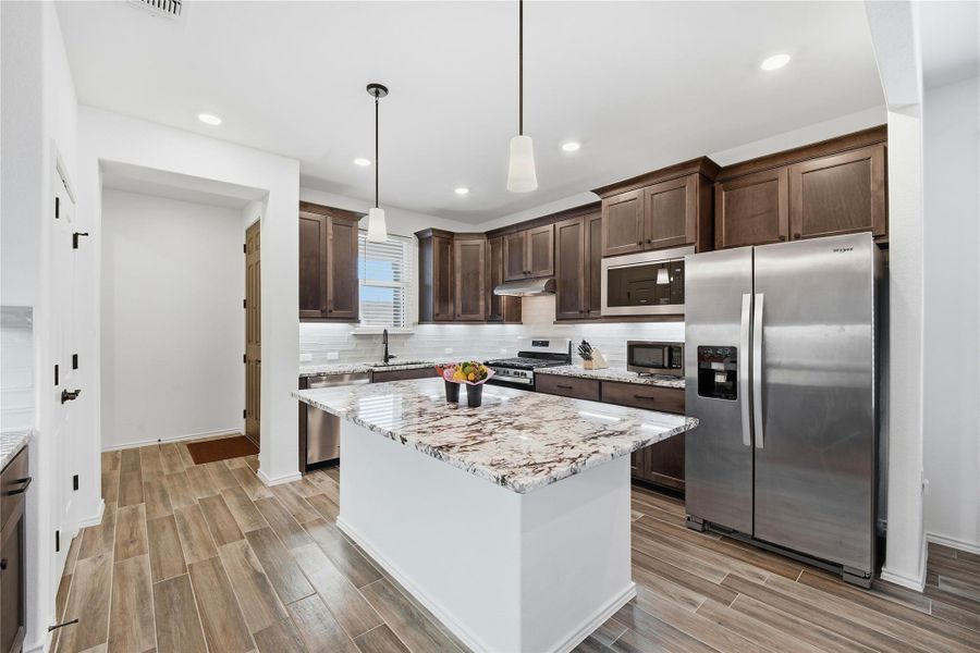 Kitchen featuring stainless steel appliances, dark wood finish cabinetry, decorative light fixtures, and wood finish floors