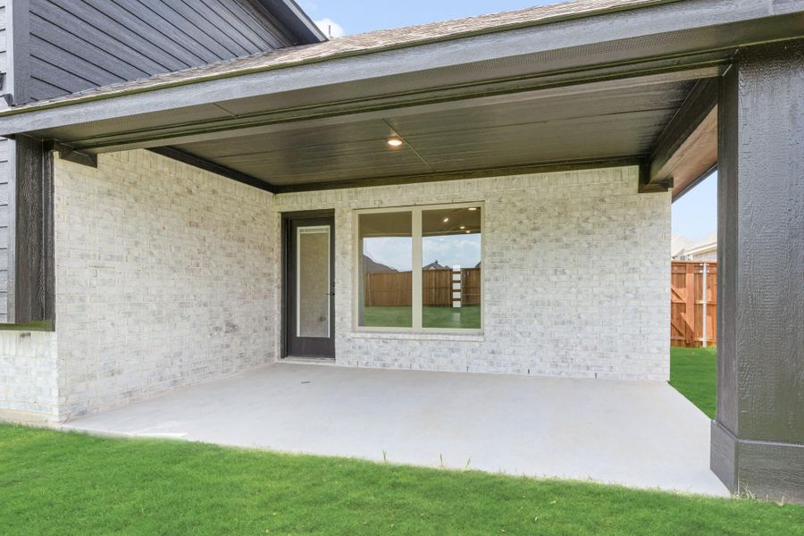 Covered back patio with concrete floor, light brick exterior, and back door leading to fenced yard