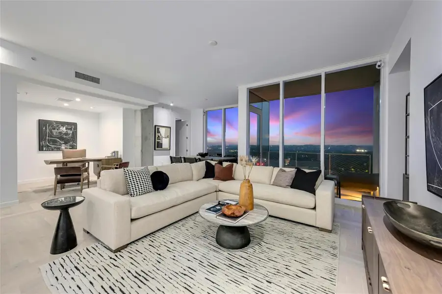 Modern elegance meets breathtaking views in this light-filled living space. Floor-to-ceiling windows frame a spectacular sunset skyline, while the open-concept design seamlessly connects the living, dining, den & kitchen areas. Neutral tones, sleek finishes, and contemporary furnishings create a sophisticated yet inviting ambiance in this newly constructed luxury residence  (Photo from previous model Residence No. 2104 on lower level)