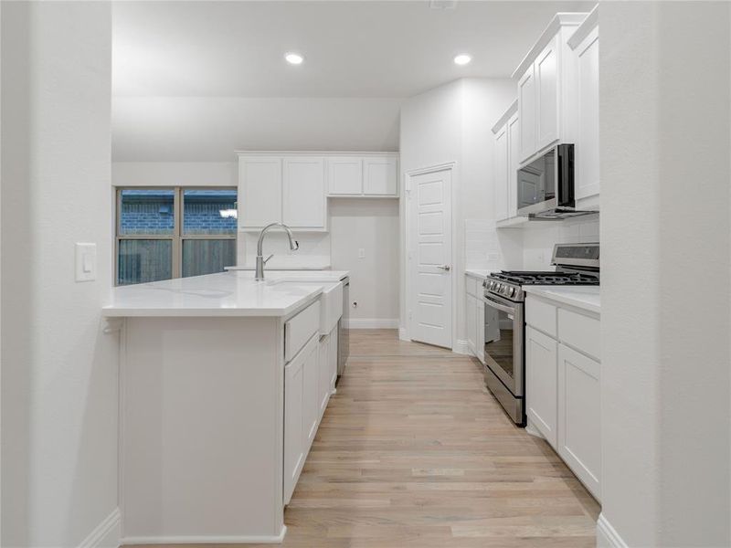 Kitchen featuring stainless steel appliances, light stone counters, decorative backsplash, white cabinets, and light wood-type flooring