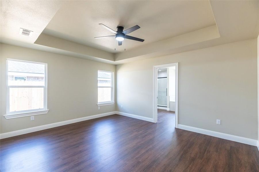 Spacious room featuring wood-finish flooring, light-toned walls, and a tray ceiling with an integrated ceiling fan