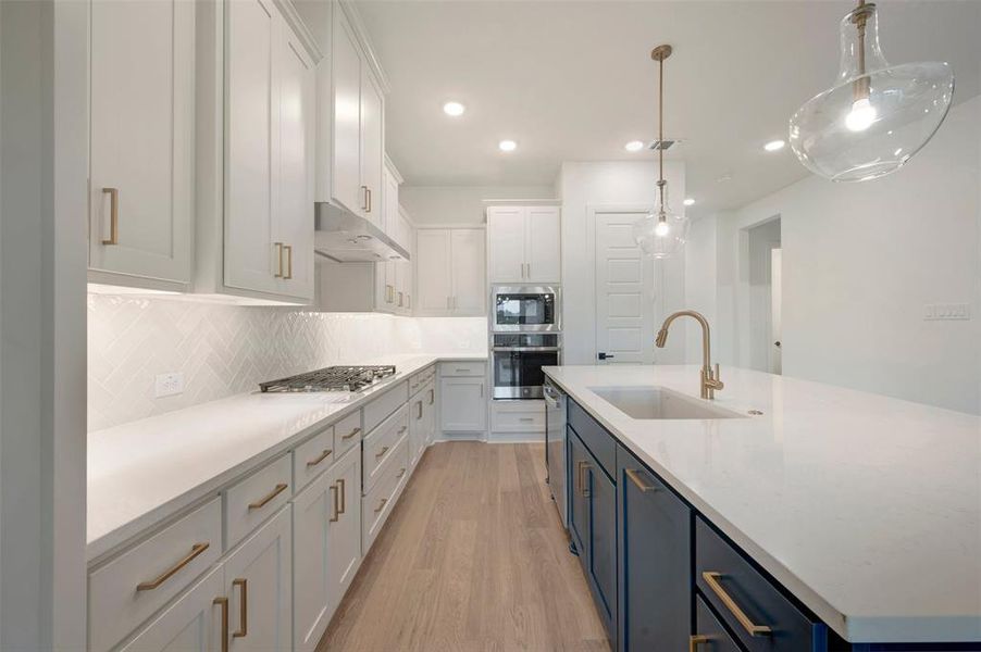 The kitchen features white cabinetry with gold-toned hardware, white countertops, and a white herringbone tile backsplash