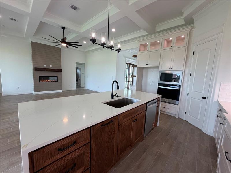 Spacious open-concept kitchen featuring a large island with a built-in sink and white countertop, dark wood-finish cabinetry, and integrated stainless steel appliances
