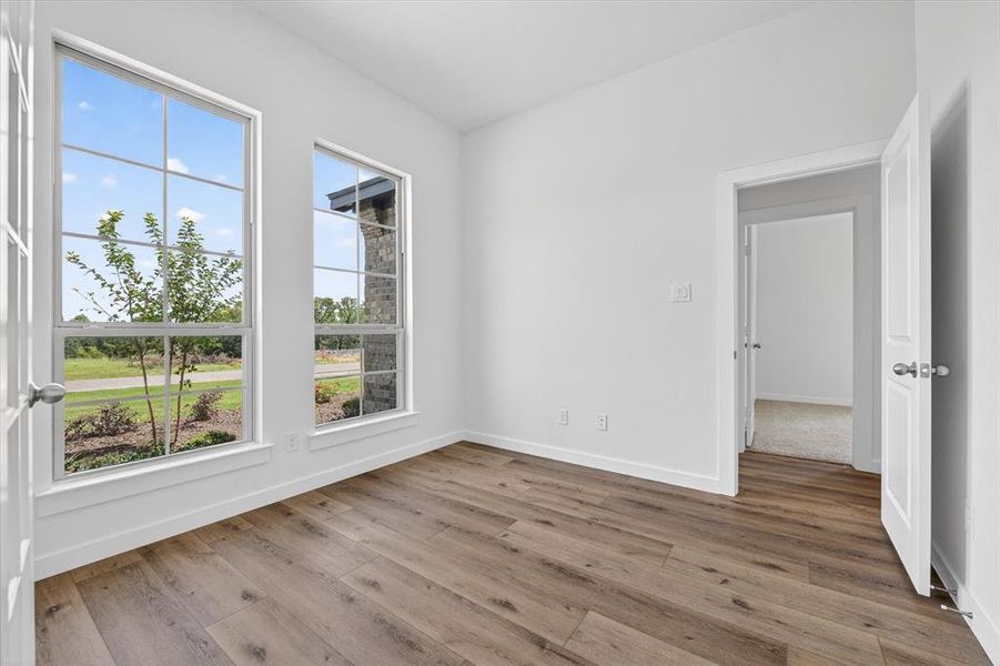 Bright room featuring two large windows, wood-finish flooring, white walls, and a white door