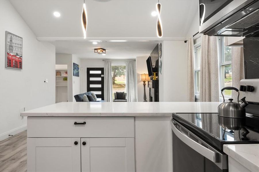 Kitchen featuring stainless steel appliances, light wood finished floors, white cabinets, open floor plan, and light stone counters Kitchen featuring stainless steel appliances, light wood finished floors, white cabinets, open floor plan, and light stone counters