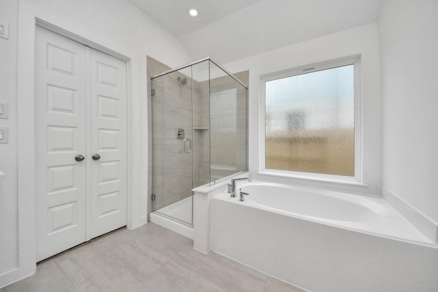 Indulge in a spa-like retreat within the confines of this primary bathroom. Delight in a spacious walk-in shower enveloped in stylish tile surround, unwind in a separate garden tub adorned with custom detailing. Sample photo of completed home with similar floor plan. Actual colors and selections may vary.