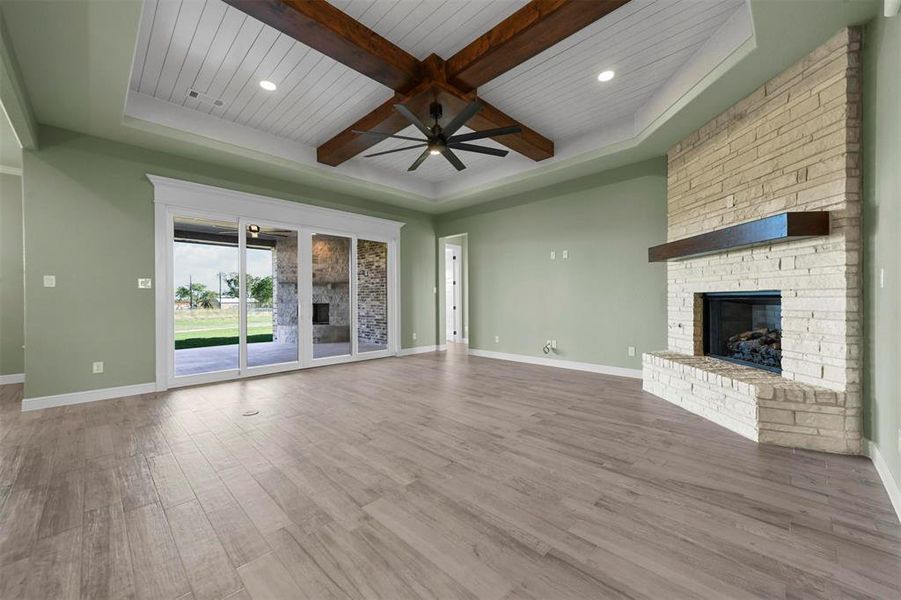 Unfurnished living room with hardwood / wood-style floors, wooden ceiling, a stone fireplace, ceiling fan, and beamed ceiling