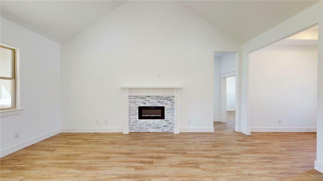 Unfurnished living room featuring high vaulted ceiling, a fireplace, light wood-style flooring, and baseboards