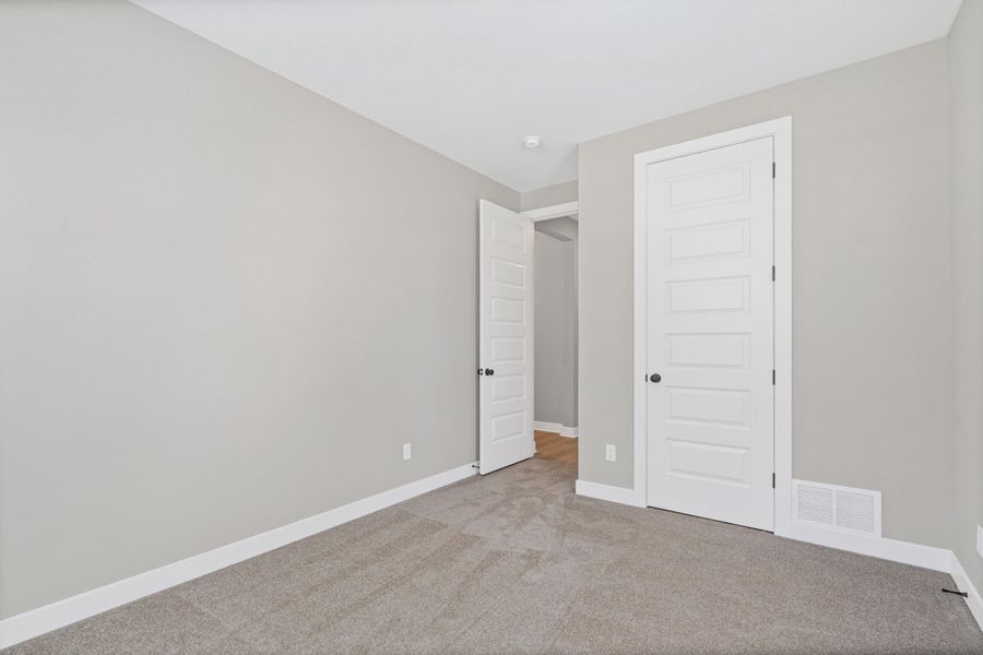Carpeted room featuring light gray walls, white trim, and two white paneled doors with matte black hardware Carpeted room featuring light gray walls, white trim, and two white paneled doors with matte black hardware