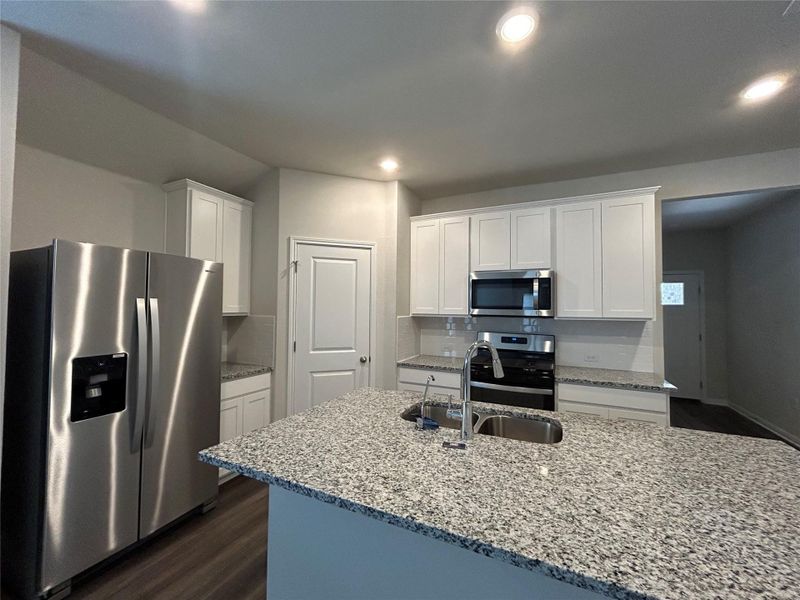 Kitchen with stainless steel appliances, dark wood-style floors, white cabinetry, recessed lighting, and light stone countertops Kitchen with stainless steel appliances, dark wood-style floors, white cabinetry, recessed lighting, and light stone countertops